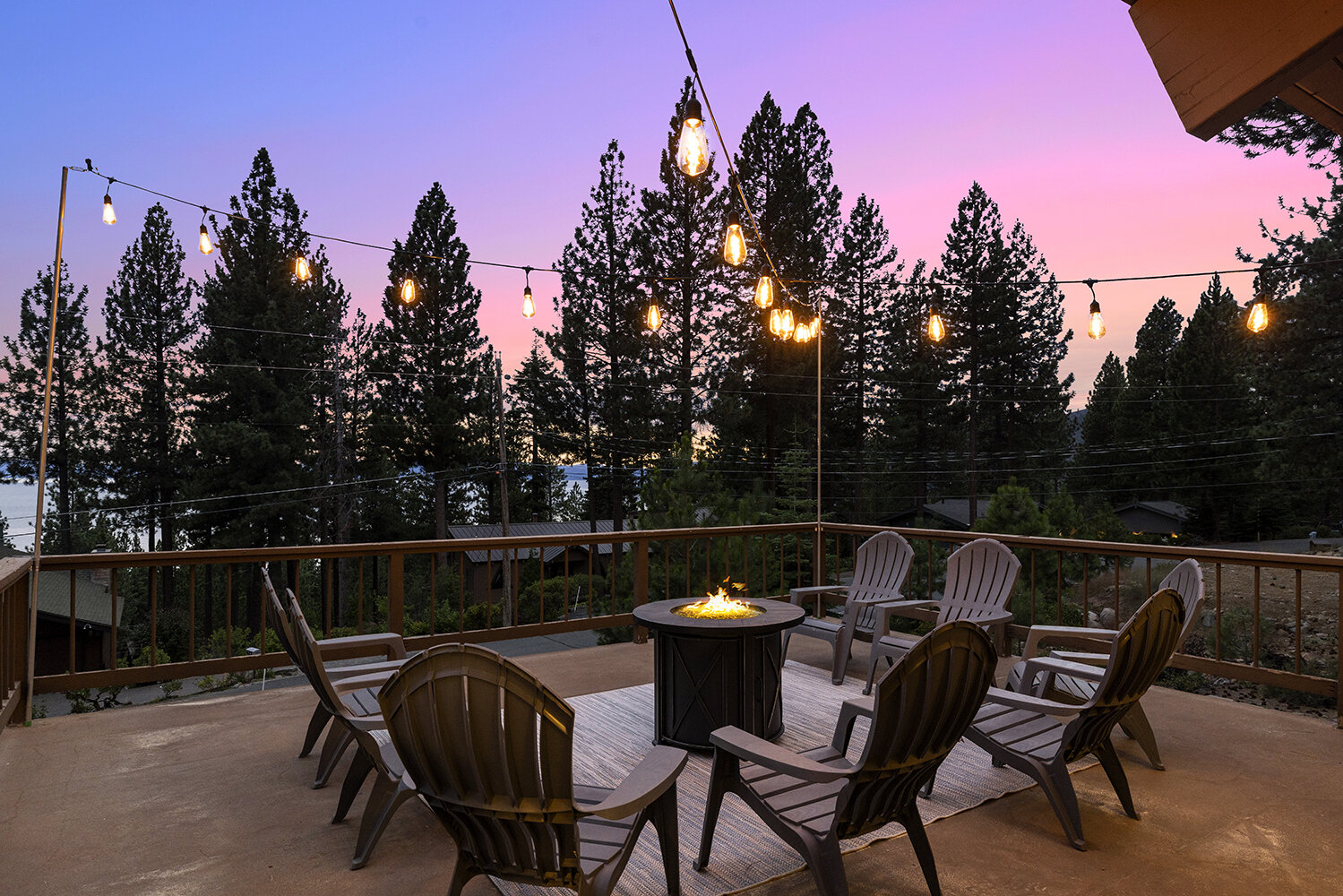 The Kinpine House deck at sunset — Adirondack chairs around the fire pit under string lights, Lake Tahoe past the pines