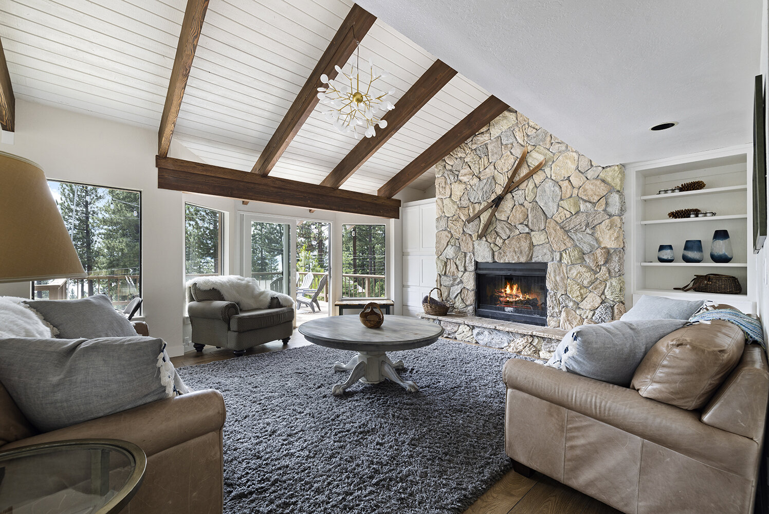 The great room at Kinpine House — stone fireplace lit under vaulted beams, sofas and forest windows