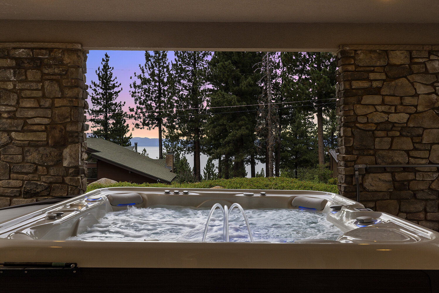The seven-person hot tub at Kinpine House, framed by stone columns with Lake Tahoe at dusk beyond